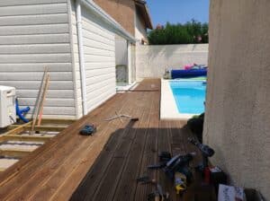 Construction d'une terrasse en bois autour d'une piscine, avec outils Makita (scie circulaire, visseuses) sur les lames fraîchement posées.